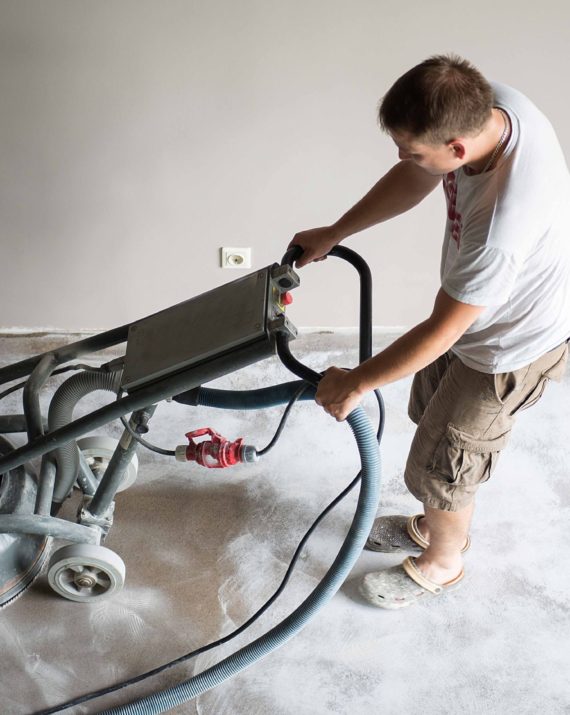 Construction worker in a family home living room that grind the concrete surface before applying epoxy flooring.Polyurethane and epoxy flooring.Concrete grinding.